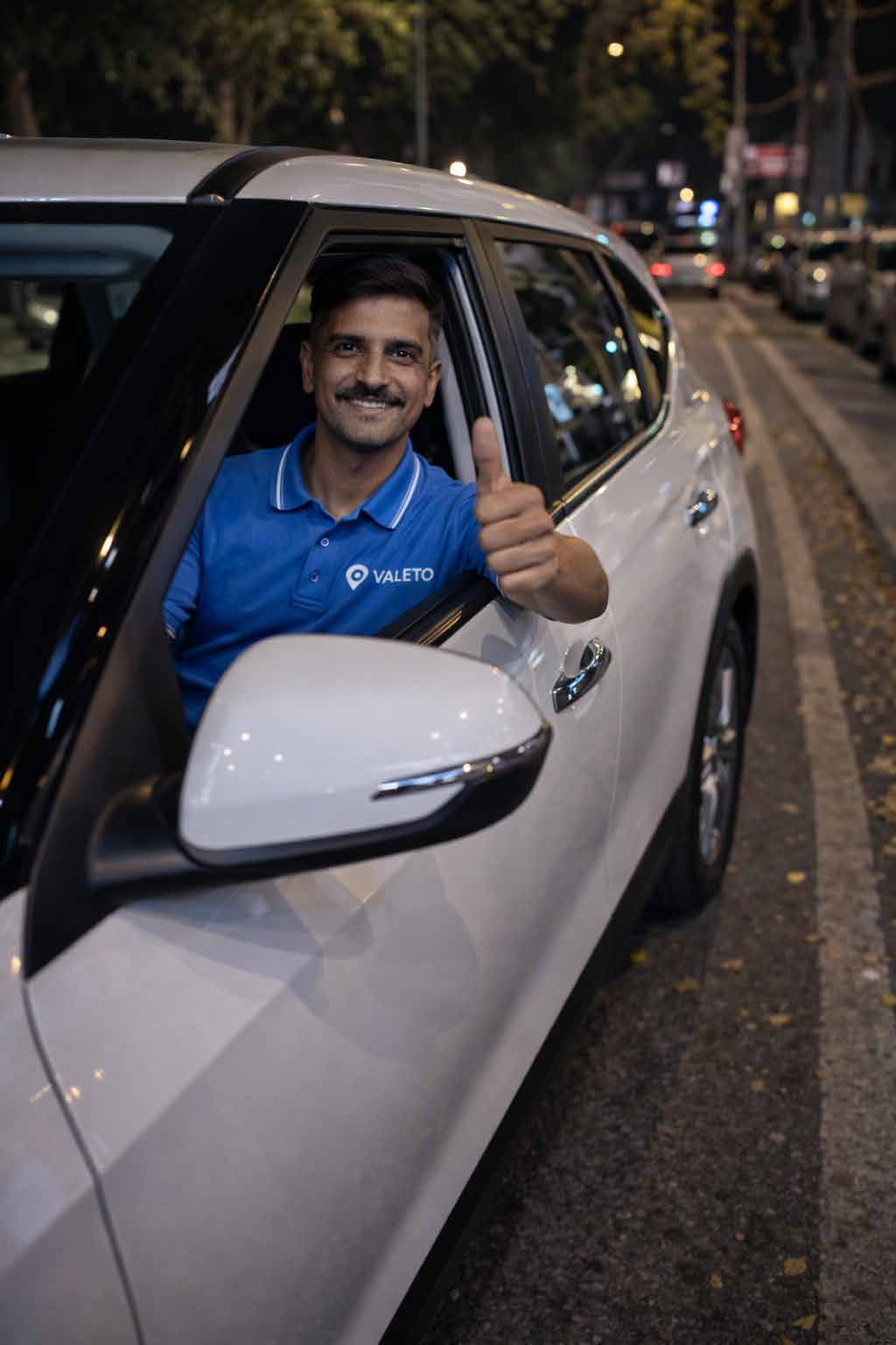 Valeto valet in branded uniform beside a client vehicle
